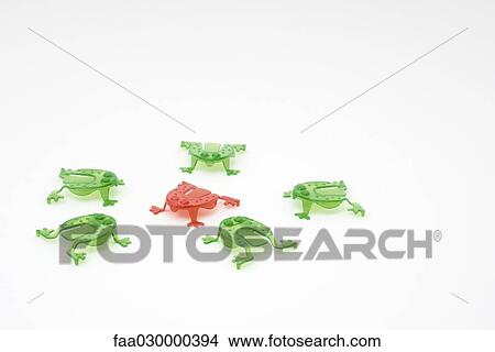 Picture - Green plastic frogs surrounding red frog in center. Fotosearch
