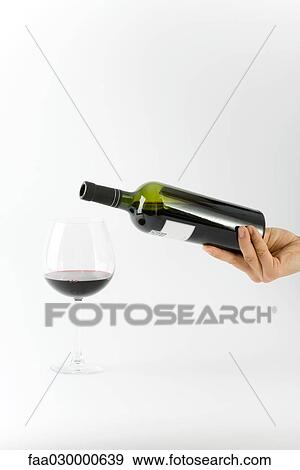 Hand holding wine bottle above glass with a small amount of red wine in it View Large Photo Image Stock Photo - Hand holding wine bottle above glass with a small amount of red wine in it. Fotosearch