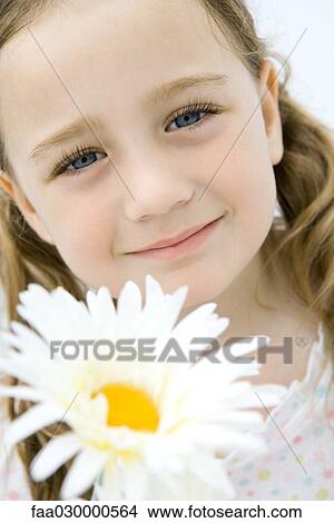 Picture - Headshot of girl smiling at camera, head tilted, flower in foreground. Fotosearch