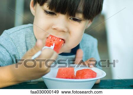 Stock Photo - Little boy eating chunks of watermelon. Fotosearch