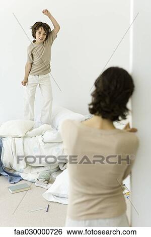 Little boy jumping on unmade bed, mother watching from doorway View Large Photo Image Stock Photograph - Little boy jumping on unmade bed, mother watching from doorway. Fotosearch