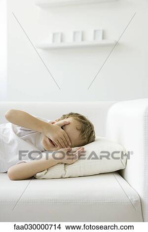 Little boy lying on sofa, hand over face, smiling View Large Photo Image Picture - Little boy lying on sofa, hand over face, smiling. Fotosearch