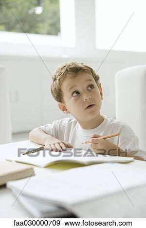 Stock Photo - Little boy sitting in front of homework, looking up. Fotosearch
