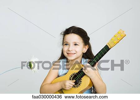 Little girl playing toy guitar, next to flower View Large Photo Image Stock Photograph - Little girl playing toy guitar, next to flower. Fotosearch