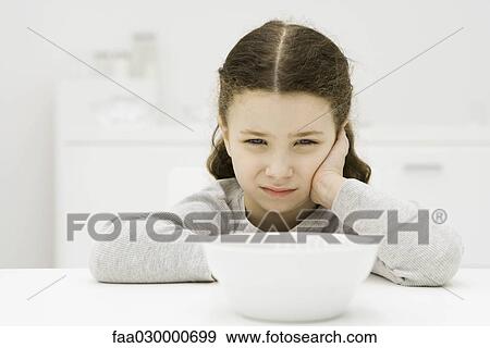 Stock Photo - Little girl sitting in front of bowl, holding head, sulking. Fotosearch