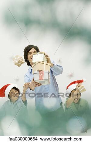 Male carrying stack of Christmas gifts, boys reaching and scattering them, smiling View Large Photo Image Picture - Male carrying stack of Christmas gifts, boys reaching and scattering them, smiling. Fotosearch