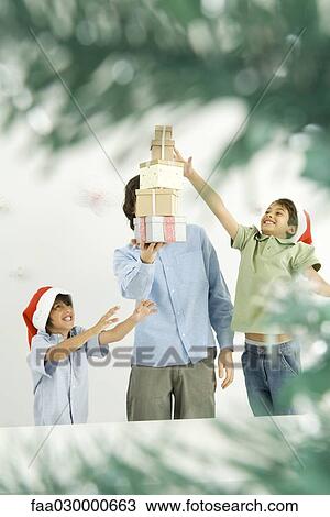 Male holding stack of Christmas gifts, two boys reaching, viewed through Christmas tree branches View Large Photo Image Stock Image - Male holding stack of Christmas gifts, two boys reaching, viewed through Christmas tree branches. Fotosearch