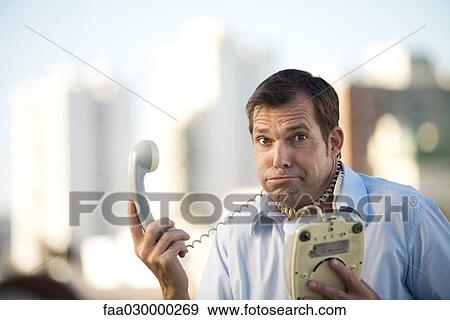 Man holding landline phone, cord wrapped around his neck, looking at camera View Large Photo Image Stock Photo - Man holding landline phone, cord wrapped around his neck, looking at camera. Fotosearch