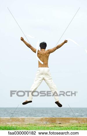 Man jumping into the air with streamers in hands, rear view, ocean horizon in background View Large Photo Image Stock Image - Man jumping into the air with streamers in hands, rear view, ocean horizon in background. Fotosearch