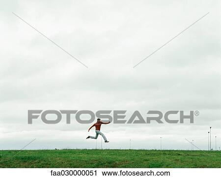 Stock Image - Man jumping on grassy field, in the distance. Fotosearch