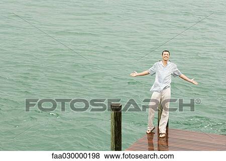 Man leaning against dock post, getting wet, arms out, smiling at camera View Large Photo Image Stock Photo - Man leaning against dock post, getting wet, arms out, smiling at camera. Fotosearch