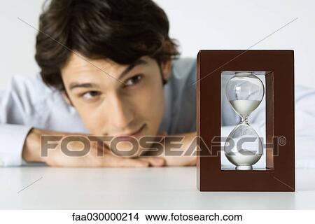 Man looking at hourglass, head resting on hands View Large Photo Image Picture - Man looking at hourglass, head resting on hands. Fotosearch
