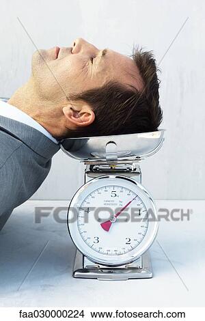 Picture - Man resting head on scale, eyes closed. Fotosearch