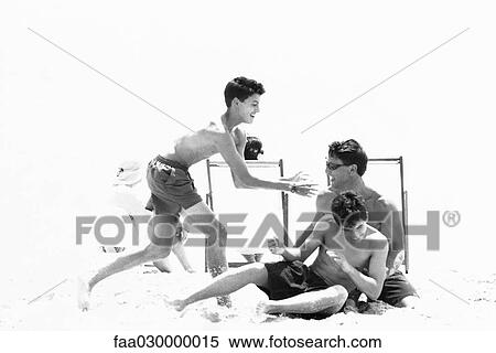 Stock Photography - Man roughhousing on beach with teenage sons, black and white. Fotosearch