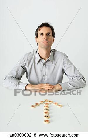 Man sitting at table, Chinese game pieces in shape of arrow pointing to him View Large Photo Image Stock Photo - Man sitting at table, Chinese game pieces in shape of arrow pointing to him. Fotosearch