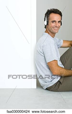 Picture - Man sitting on floor, listening to headphones, smiling at camera. Fotosearch