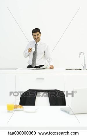 Man standing at kitchen counter with coffee in hand, smiling at camera View Large Photo Image Stock Image - Man standing at kitchen counter with coffee in hand, smiling at camera. Fotosearch