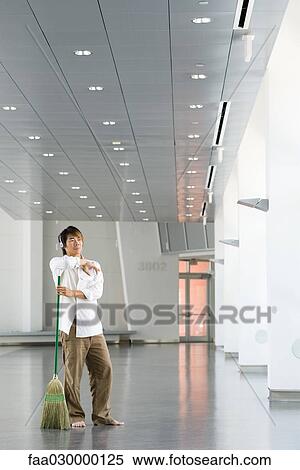 Man standing in lobby with broom, listening to headphones View Large Photo Image Stock Photography - Man standing in lobby with broom, listening to headphones. Fotosearch