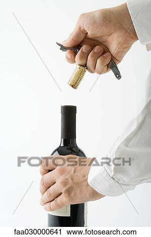 Stock Image - Man uncorking bottle of wine, cropped view of hands. Fotosearch