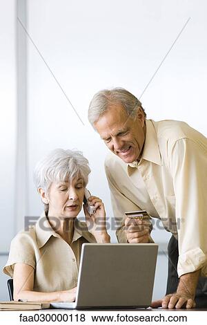 Mature couple making credit card purchase, using laptop and cell phone View Large Photo Image Stock Photo - Mature couple making credit card purchase, using laptop and cell phone. Fotosearch