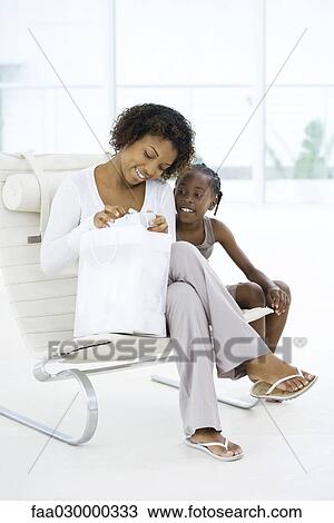 Mother and daughter sitting together, woman opening gift, both smiling View Large Photo Image Stock Image - Mother and daughter sitting together, woman opening gift, both smiling. Fotosearch