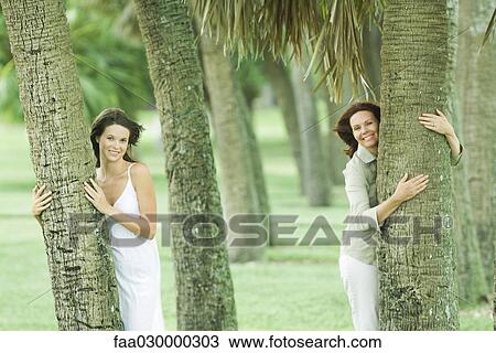 Mother and teen daughter hugging tree trunks, smiling at camera View Large Photo Image Stock Image - Mother and teen daughter hugging tree trunks, smiling at camera. Fotosearch