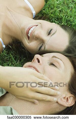Stock Photography - Mother and teen daughter lying on the ground, girl touching woman's face, cropped view. Fotosearch