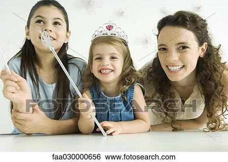 Mother and two daughters, smiling at camera, younger girl wearing tiara and holding wand View Large Photo Image Stock Photograph - Mother and two daughters, smiling at camera, younger girl wearing tiara and holding wand. Fotosearch