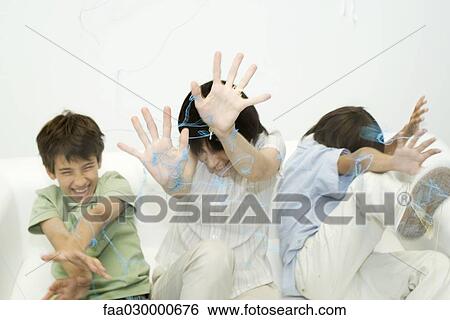 Stock Photograph - Mother and two sons being sprayed with spray string, hands raised, laughing. Fotosearch