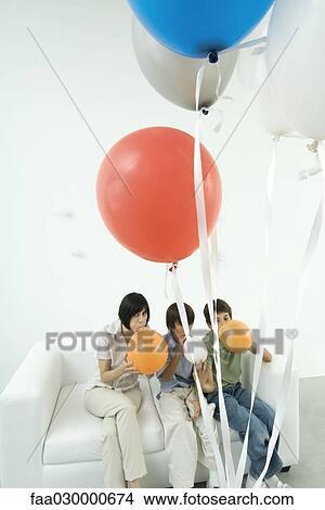 Mother and two sons sitting on sofa, inflating balloons View Large Photo Image Picture - Mother and two sons sitting on sofa, inflating balloons. Fotosearch
