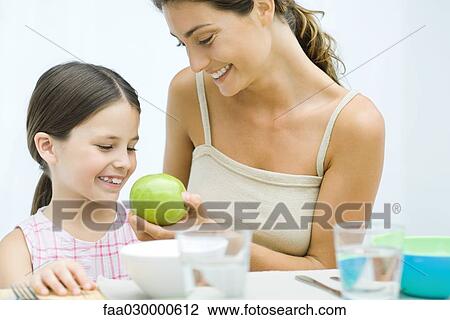 Mother giving daughter an apple, both smiling View Large Photo Image Stock Image - Mother giving daughter an apple, both smiling. Fotosearch