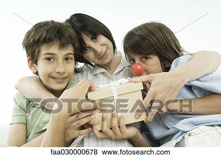 Mother sitting with two sons, holding gift, smiling at camera View Large Photo Image Stock Photo - Mother sitting with two sons, holding gift, smiling at camera. Fotosearch
