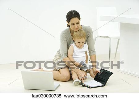 Mother with toddler on lap, looking at agenda, laptop nearby View Large Photo Image Stock Photography - Mother with toddler on lap, looking at agenda, laptop nearby. Fotosearch