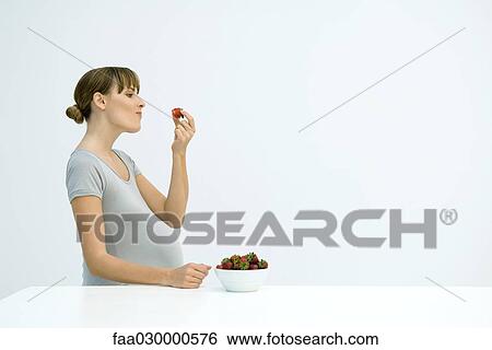 Stock Photograph - Pregnant woman eating strawberries from a bowl, side view. Fotosearch