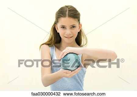 Stock Image - Preteen girl holding small globe in hands, smiling at camera. Fotosearch