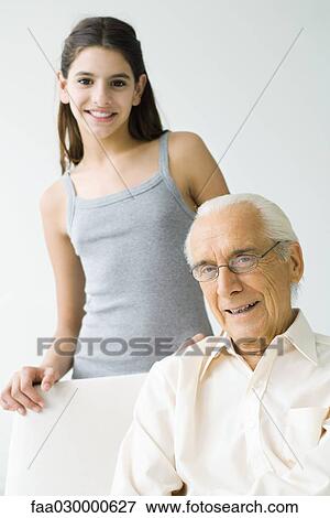 Preteen girl standing behind grandfather, both smiling at camera View Large Photo Image Stock Photo - Preteen girl standing behind grandfather, both smiling at camera. Fotosearch