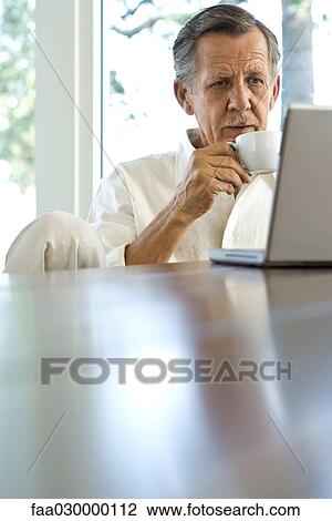 Senior man drinking coffee and using laptop View Large Photo Image Stock Image - Senior man drinking coffee and using laptop. Fotosearch
