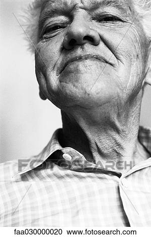 Stock Image - Senior man, looking at camera, low angle view, black and white, portrait. Fotosearch