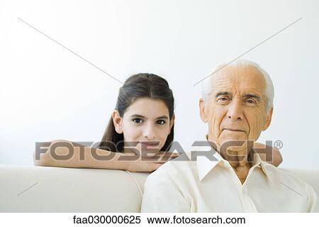 Stock Photography - Senior man smiling at camera, preteen granddaughter looking over his shoulder. Fotosearch