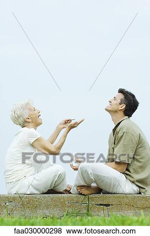 Senior woman and adult son sitting face to face on the ground, sharing takeout food, laughing View Large Photo Image Stock Photo - Senior woman and adult son sitting face to face on the ground, sharing takeout food, laughing. Fotosearch