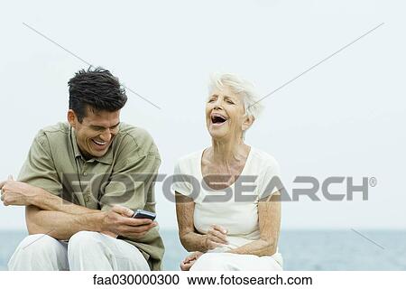 Senior woman and adult son sitting side by side outdoors, laughing, man holding cell phone View Large Photo Image Stock Image - Senior woman and adult son sitting side by side outdoors, laughing, man holding cell phone. Fotosearch