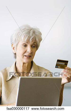 Senior woman making on-line purchase, looking at credit card View Large Photo Image Stock Photo - Senior woman making on-line purchase, looking at credit card. Fotosearch