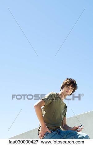 Stock Photo - Teen boy listening to MP3 player, smilng at camera. Fotosearch