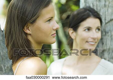 Teen girl and woman leaning against tree trunks, looking away, smiling View Large Photo Image Stock Image - Teen girl and woman leaning against tree trunks, looking away, smiling. Fotosearch