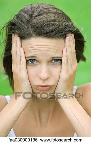 Stock Photograph - Teen girl holding face in hands, furrowing brow, close-up. Fotosearch