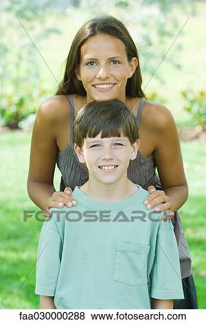 Teen girl standing behind younger brother, resting her chin on his head, both smiling at camera View Large Photo Image Stock Photo - Teen girl standing behind younger brother, resting her chin on his head, both smiling at camera. Fotosearch