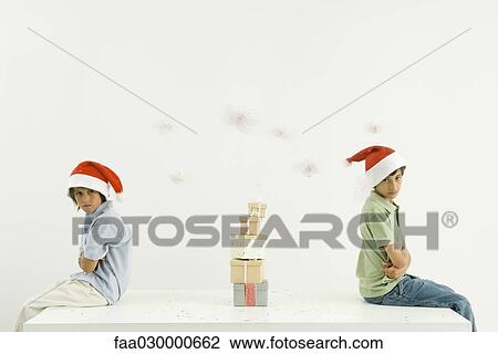 Two brothers sitting back to back with arms folded, Christmas gifts stacked between them, one looking at camera View Large Photo Image Stock Image - Two brothers sitting back to back with arms folded, Christmas gifts stacked between them, one looking at camera. Fotosearch