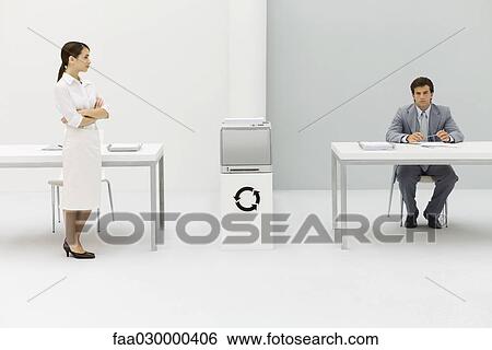 Stock Photograph - Two professionals in office, woman with arms folded, man looking at camera, circular arrow symbol between them. Fotosearch