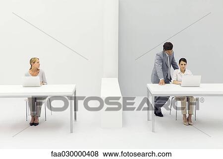 Two women working in office, man standing behind one with his hand on her shoulder View Large Photo Image Stock Photo - Two women working in office, man standing behind one with his hand on her shoulder. Fotosearch