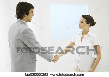 Stock Image - Two young professionals shaking hands, smiling. Fotosearch